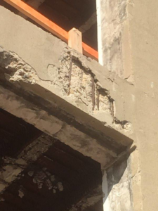 Close-up of a concrete beam showing exposed rebar and damage, indicating a structural repair by Kemna Restoration & Construction in Indianapolis, IN.