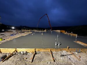A concrete foundation pour in progress at night with a pump truck by R and R contractors in Rogers, AR.