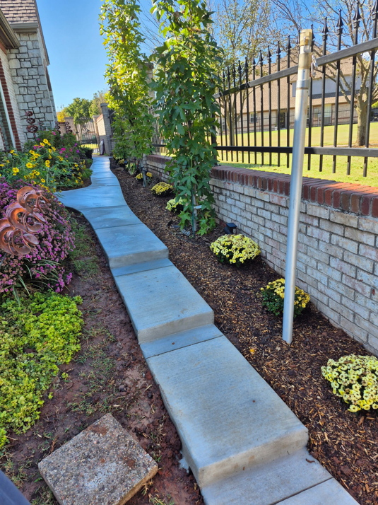 A finished concrete pathway with steps, bordered by landscaping, installed by All American Concrete in Crescent, OK.