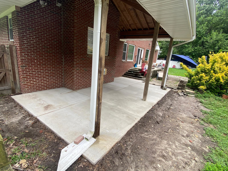 A new concrete patio installed under a covered porch of a brick house by McGhee's Concrete in Chesapeake, VA.