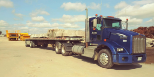 A blue R A Seaton Contractor Services flatbed truck transporting large concrete slabs in Rockford, IL.