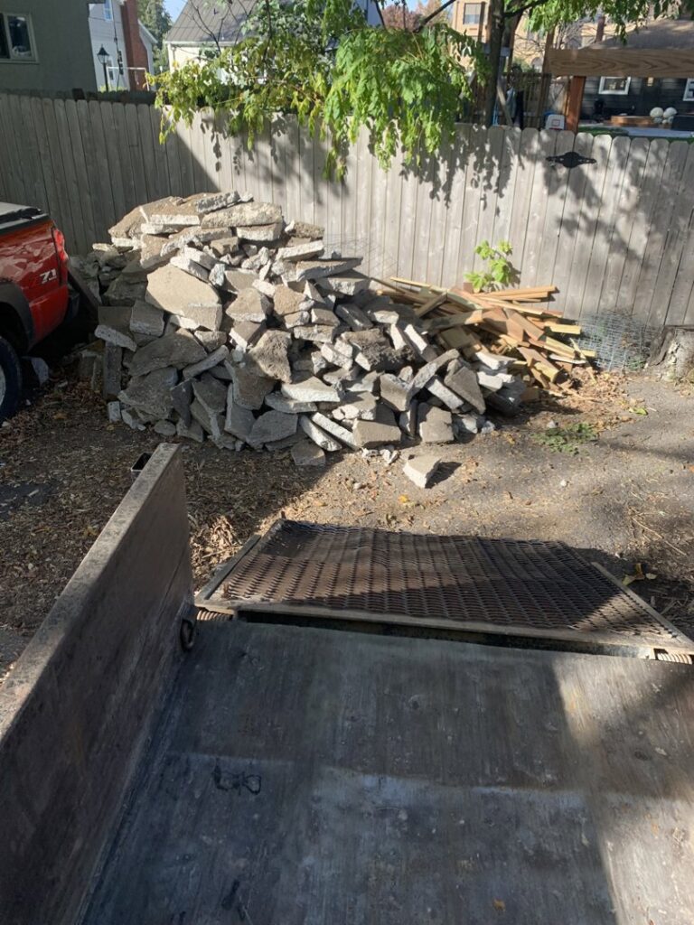 A large pile of broken concrete and wood debris next to a junk removal trailer from Mr. Groundhog Disposal and Services in Bloomington, MN.