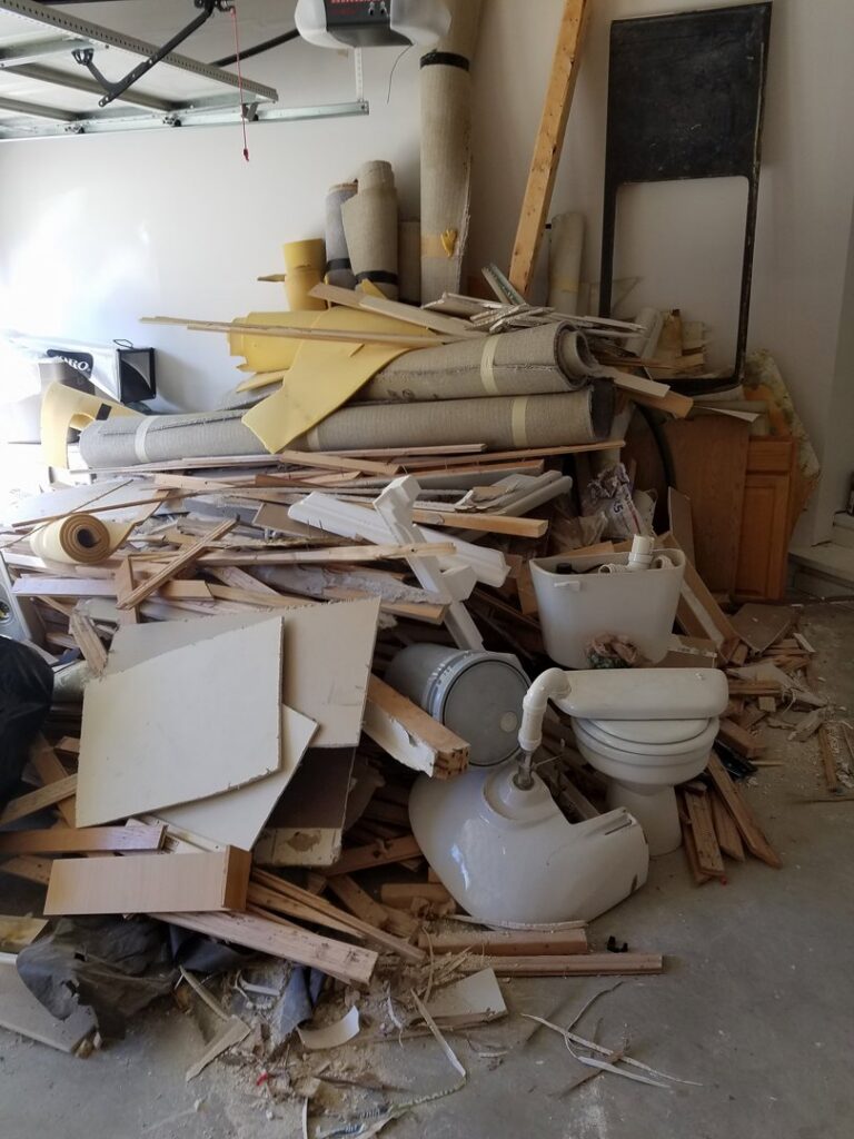 A large pile of construction debris, old carpet, wood, and a toilet in a garage, ready for Junk Unlimited Junk Removal in Laurel, MD.