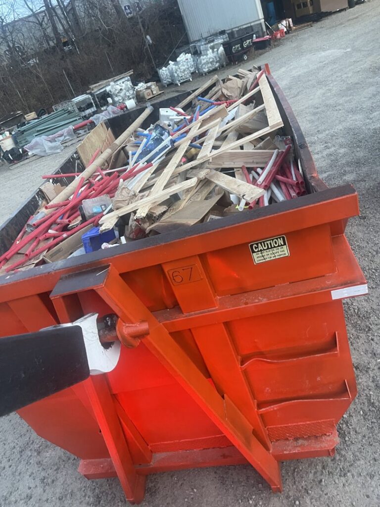 An orange dumpster filled with construction debris, including wood and pipes, for removal by Lil Man W/A Can LLC in Columbus, OH.