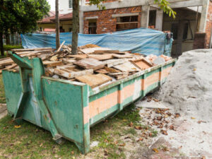 A large green dumpster filled with wood and construction debris, indicating a cleanup service by Trashouts Junk Removal in Pembroke Pines, FL.