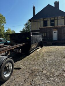 A black roll-off dumpster being placed or picked up at a property undergoing renovation for construction debris removal by Wagners Property Services LLC in Canton, OH.