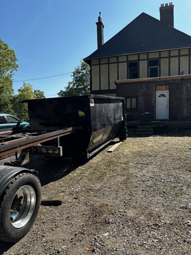 A black roll-off dumpster being placed or picked up at a property undergoing renovation for construction debris removal by Wagners Property Services LLC in Canton, OH.