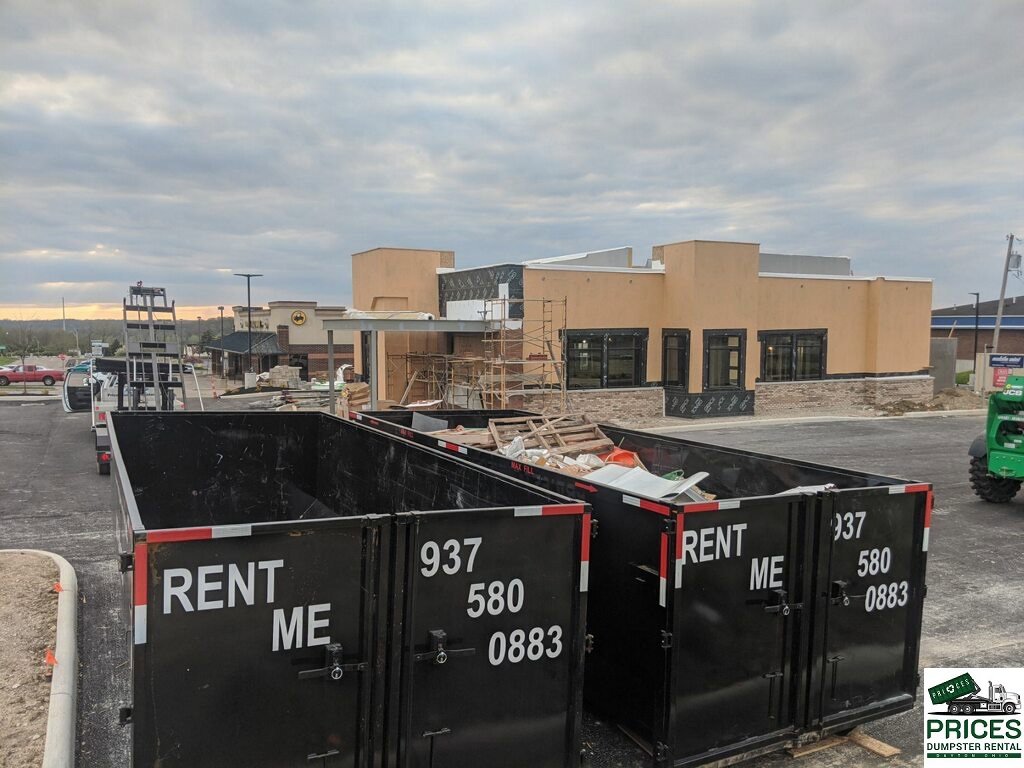 Two dumpsters, one partially filled with construction debris, at a commercial site in Dayton, OH, by Big Reds Dumpster Rental.