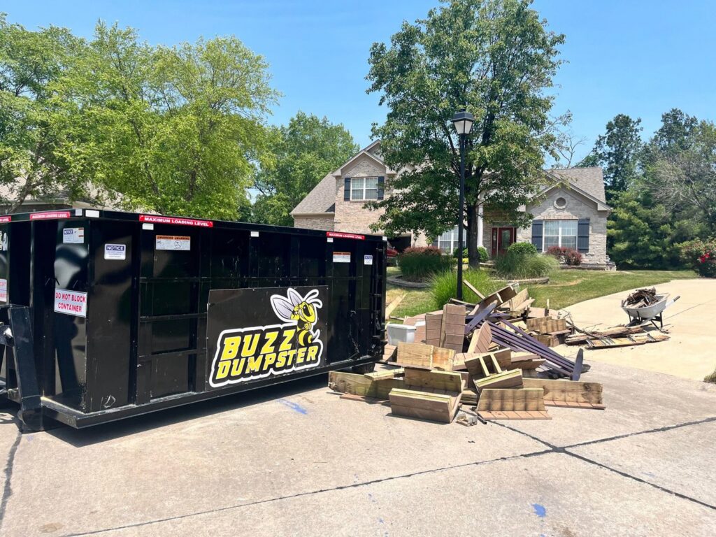 A Buzz Dumpster & Junk Removal container next to a pile of construction debris for removal in Troy, MO.