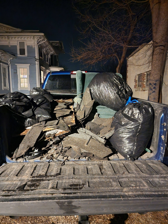 A pickup truck bed filled with construction debris, including shingles and trash bags, by Curtis Rose Companies LLC in Janesville, WI.