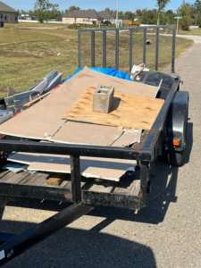 A utility trailer loaded with construction debris including drywall, wood, and a concrete block, for removal by Resilient Trash and Cleaning LLC in New Orleans, LA.