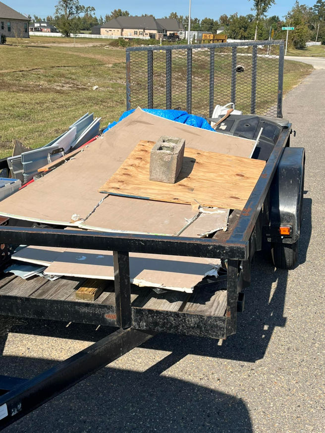 A utility trailer loaded with construction debris including drywall, wood, and a concrete block, for removal by Resilient Trash and Cleaning LLC in New Orleans, LA.