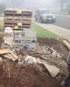 A pile of construction debris, wooden pallets, and concrete blocks on a dirt patch, ready for removal by Junk Away & Cleaning in Sacramento, CA.