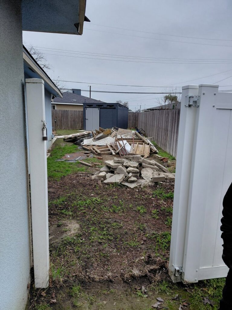 A large pile of construction debris, including wood and concrete, in a backyard, ready for removal by Valley Haul Off LLC in Visalia, CA.