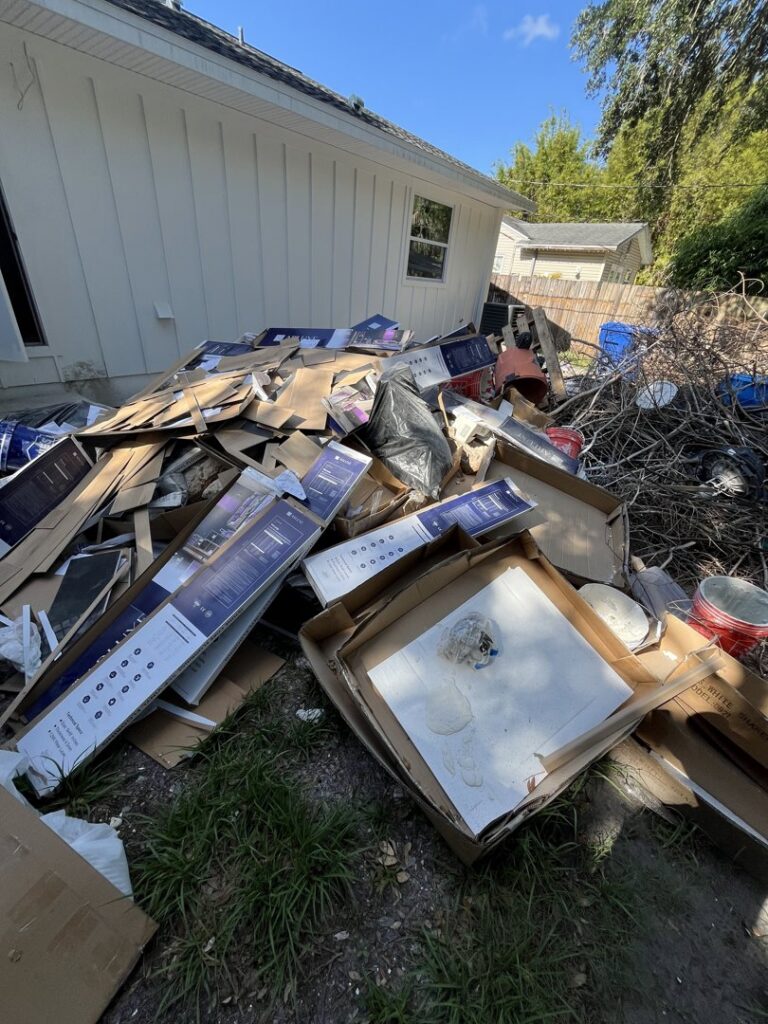 A large pile of construction debris and cardboard boxes next to a house, ready for removal by Lightning Bay Junk Removal in Tampa, FL.