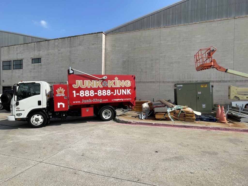 A Junk King Plano, TX truck parked next to a pile of construction debris and general junk at a job site.