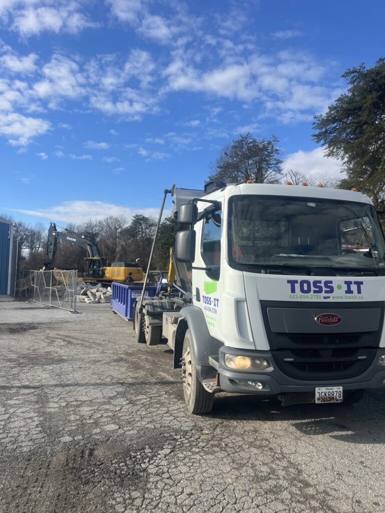 A Toss-It truck with a dumpster at a construction site with an excavator in the background in Glen Burnie, MD.