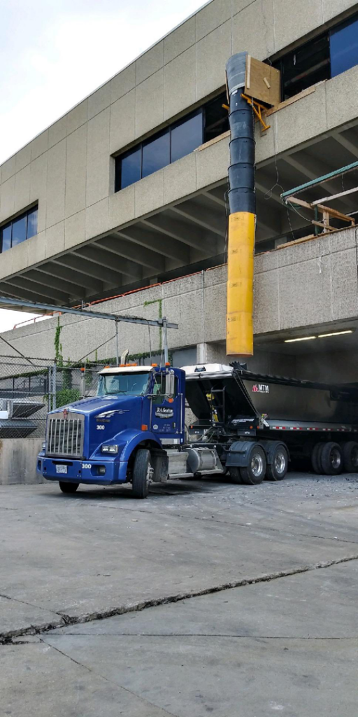 A blue semi-truck and dump trailer collecting construction debris from a building by R A Seaton Contractor Services in Rockford, IL.