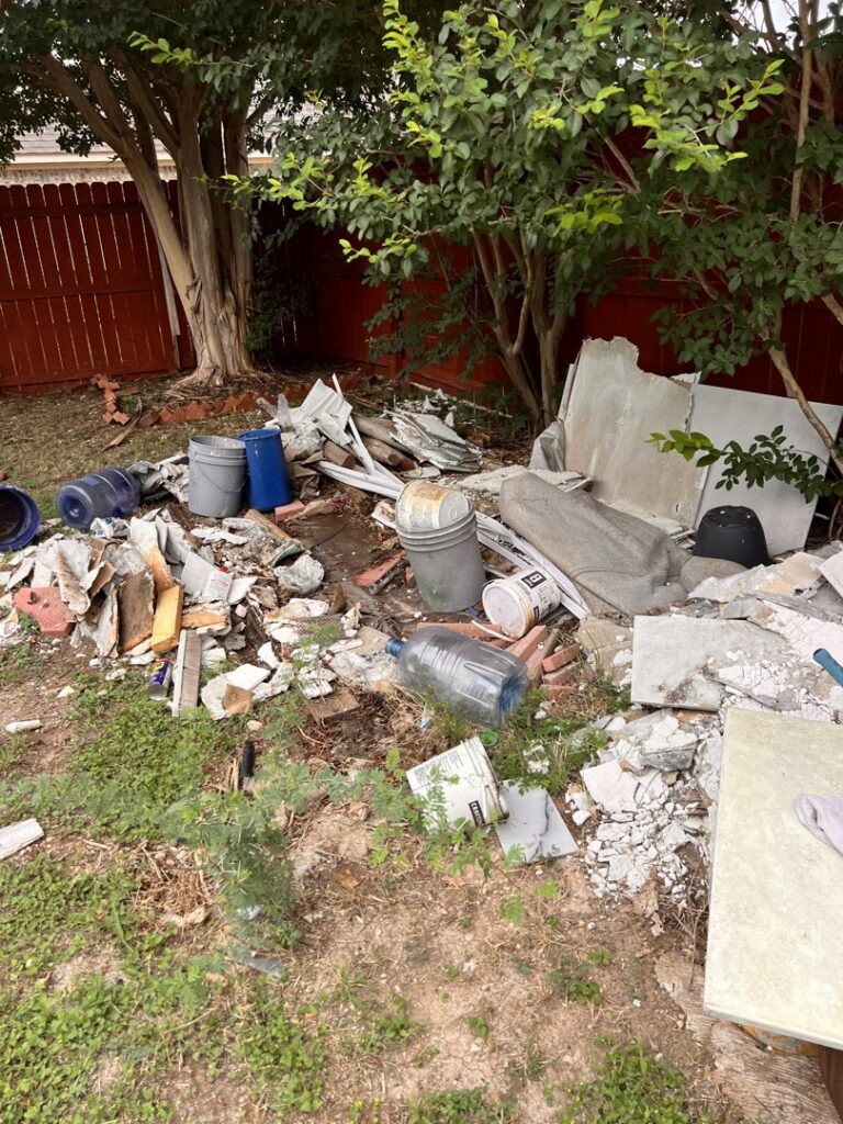 A pile of construction and demolition debris, including concrete and tiles, in a backyard for removal by SATX Junk-A-Haulics in San Antonio, TX.