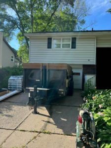 A dump trailer parked in a driveway with building materials for a construction project by CRT Dump Trailer Rentals in Prior Lake, MN.