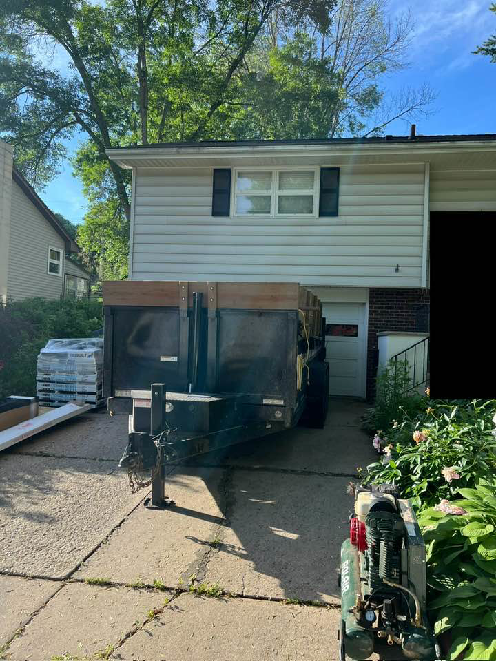 A dump trailer parked in a driveway with building materials for a construction project by CRT Dump Trailer Rentals in Prior Lake, MN.