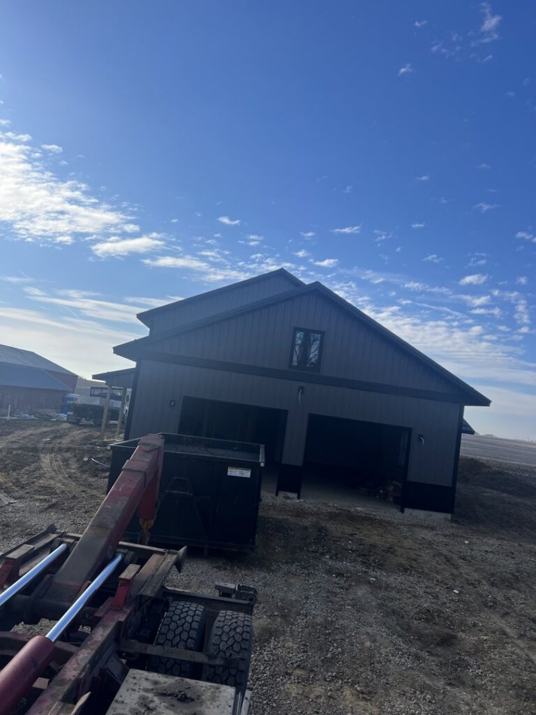 A NID Dumpster Rental truck placing a black dumpster at a construction site in Nashua, IA for debris removal.