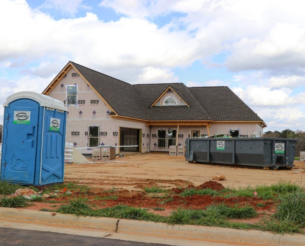 A construction site featuring a Martin Environmental roll-off dumpster and portable toilet in Dothan, AL.