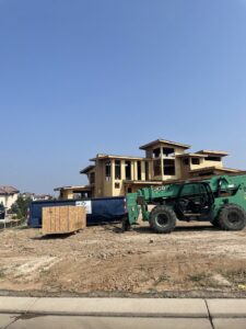 A blue dumpster and a telehandler at a construction site for a large house, used for junk removal by Discount Dumpster in Naples, FL.
