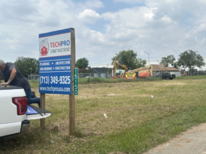 A construction site with a TechPro Constructions sign, an excavator, and a lift in Houston, TX, indicating general contractor services.