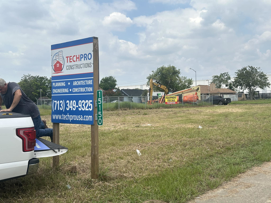 A construction site with a TechPro Constructions sign, an excavator, and a lift in Houston, TX, indicating general contractor services.