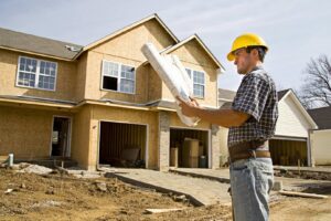 A construction worker in a hard hat reviewing blueprints in front of a new home under construction by AKN Design Group in Fort Worth, TX.