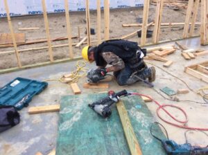 A construction worker cutting wood for framing on a concrete slab, demonstrating work by Texas Wounded Veterans Builders and Contractors in McKinney, TX.