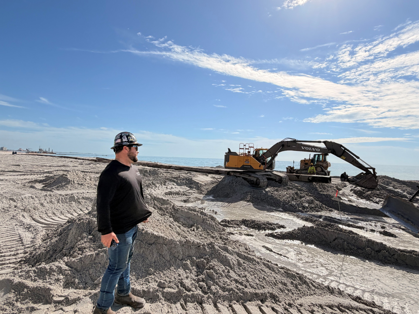 A construction worker overseeing an excavator and heavy machinery on a beach project for Gator Dredging in Clearwater, FL.