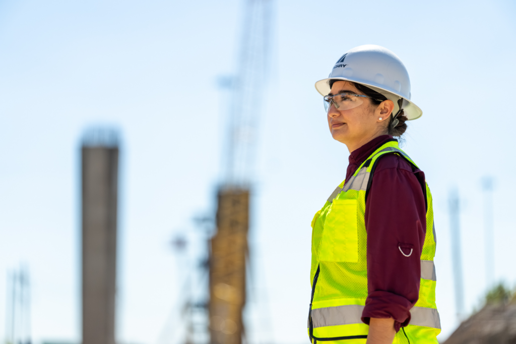 A female construction worker in a hard hat and safety vest on a job site for Zachry Construction Corporation in San Antonio, TX.
