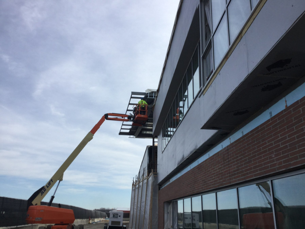 A construction worker on a lift installing exterior panels on a building for Combs Interior Specialties in Columbus, OH.
