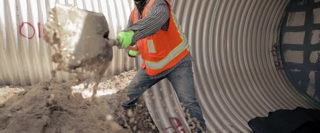 A construction worker shoveling dirt inside a large pipe during installation for Sendero Industries in Houston, TX.