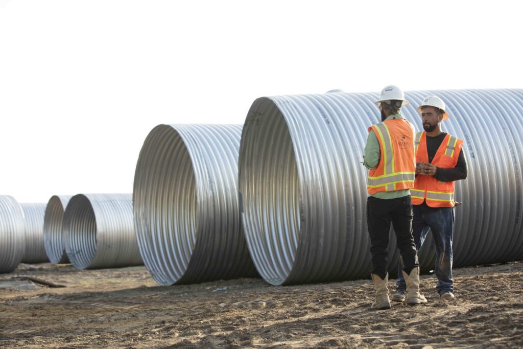 Two construction workers in safety gear inspecting large corrugated pipes on a job site for Sendero Industries in Houston, TX.