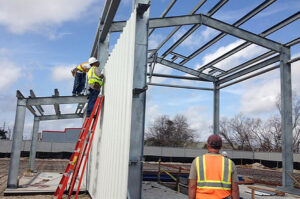 Construction workers on a ladder installing siding panels on a metal frame structure, a service by ACE Roofing & Construction in Ruskin, FL