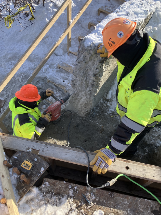 Construction workers using a jackhammer to break concrete during site preparation by Northeast-Paving in Bangor, ME