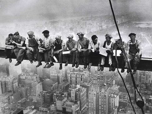 Construction workers having lunch on a steel beam high above a city, representing the work of Behar Construction in Miami, FL