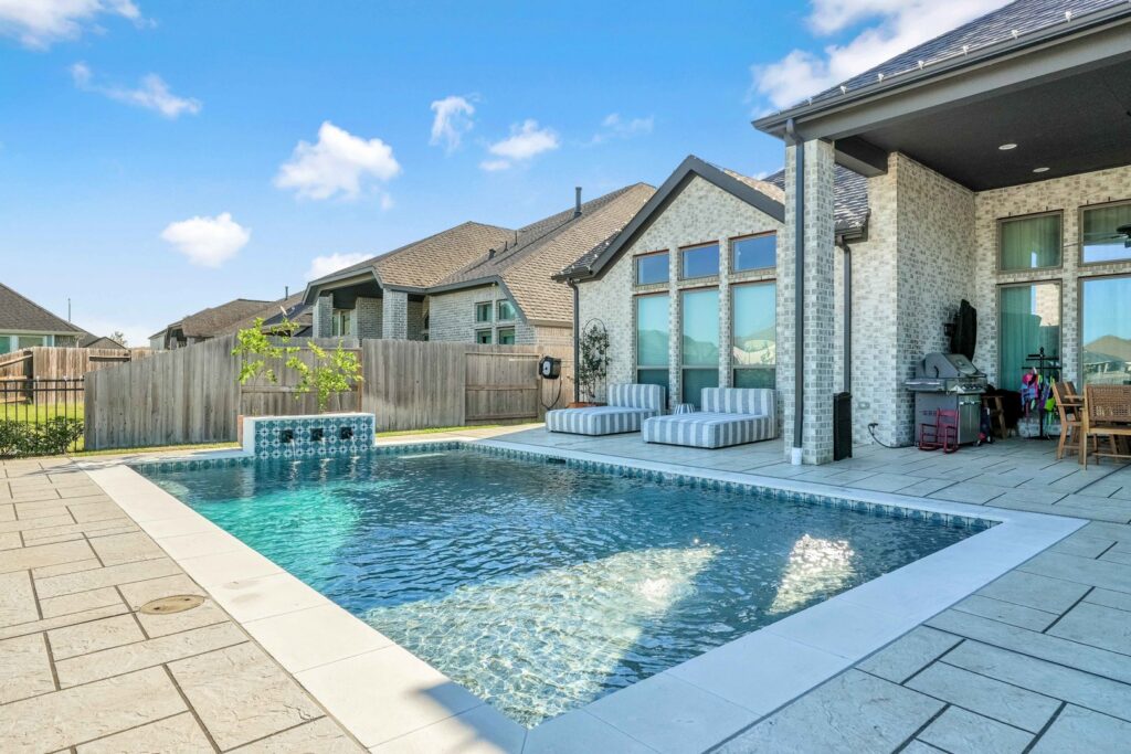 A contemporary backyard featuring a rectangular pool, spacious patio, and lounge furniture by Limitless Custom Pools and Backyards in Houston, TX.