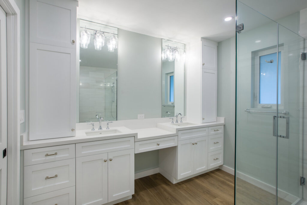 A contemporary bathroom featuring a double vanity with white cabinets and a glass shower by Madison Construction Group, Inc. in Miami, FL