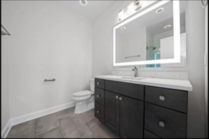 A contemporary bathroom featuring a dark wood vanity, illuminated mirror, and tiled floor by Revival Home Remodeling in Chicago, IL.