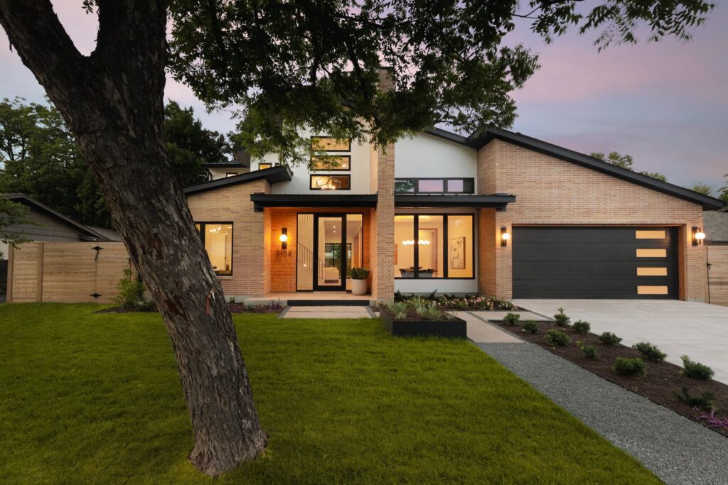 A contemporary brick and white facade home featuring a modern garage door and landscaping by Stone Acorn Builders in Bellaire, TX.