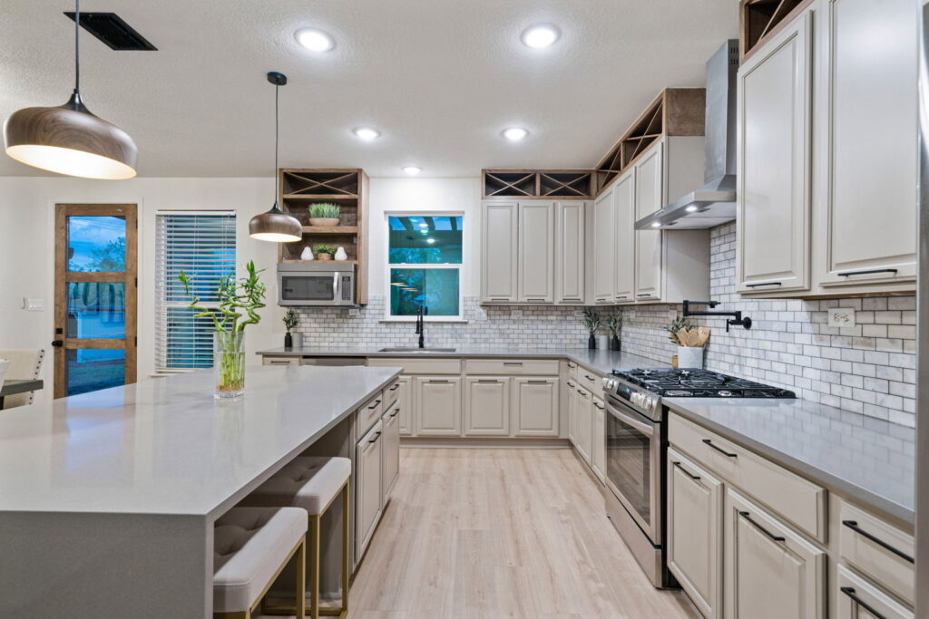 A contemporary kitchen design with light cabinetry, a large island, and subway tile backsplash by HomeNovate in San Antonio, TX.