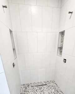 A contemporary shower design with large white wall tiles, a pebble mosaic floor, and built-in niches by Brian's Tiles in Duluth, MN.