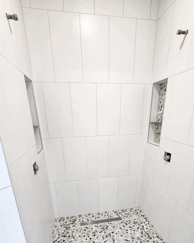 A contemporary shower design with large white wall tiles, a pebble mosaic floor, and built-in niches by Brian's Tiles in Duluth, MN.