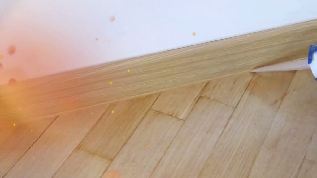 A contractor applying sealant along the baseboard and newly installed hardwood floor, a service by NV Floors LLC in Pittsburgh, PA.