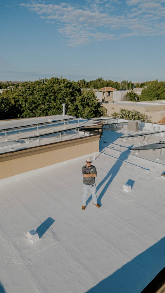 A contractor standing on a newly coated white flat roof, showcasing a completed project by Campos & Son Roofing and Construction in El Paso, TX