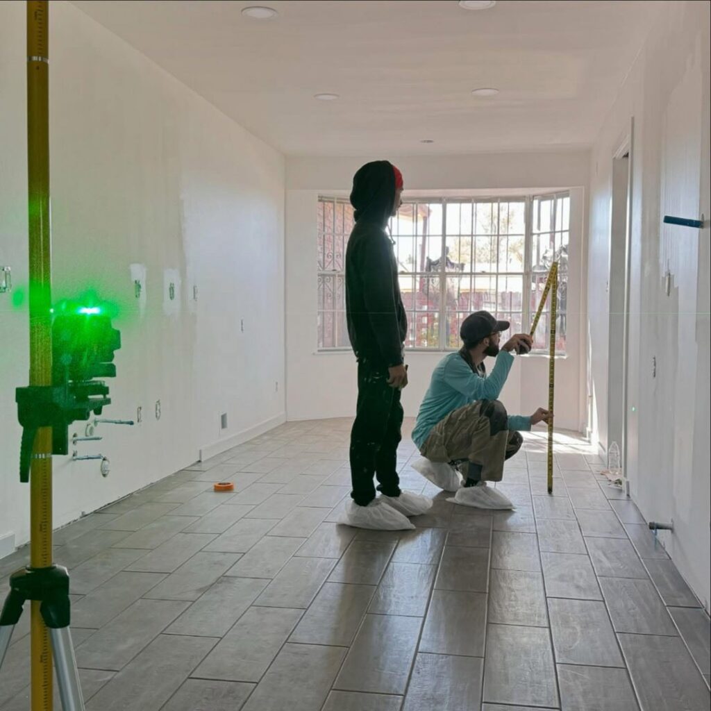 General contractors using a laser level and measuring tape in a room with new flooring during a remodel by Forged Builds Custom Remodels in El Paso, TX.